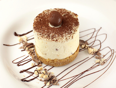 A malted cheesecake with a chocolate chip cookie base, finished with a cocoa coating and garnished with chocolate malted balls.